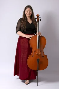 Cellist in a red skirt standing beside her cello, studio portrait
