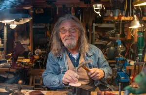 Craftsman with long grey hair working leather at his workshop bench