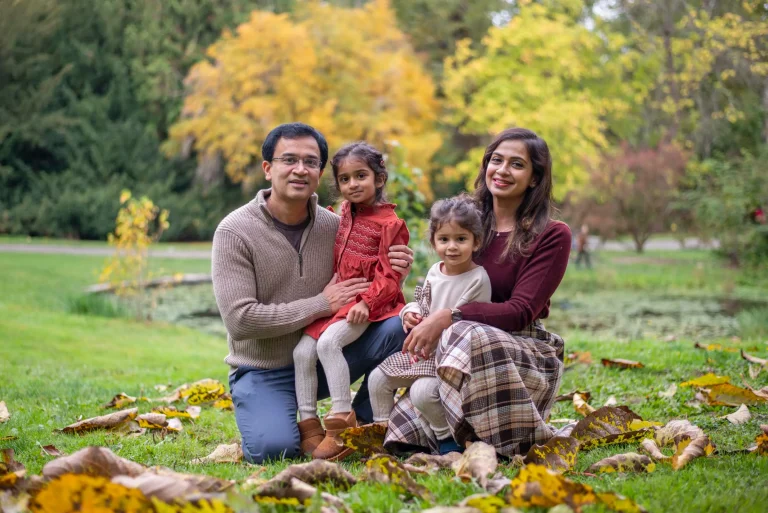 Family of four kneeling on autumn leaves in a park