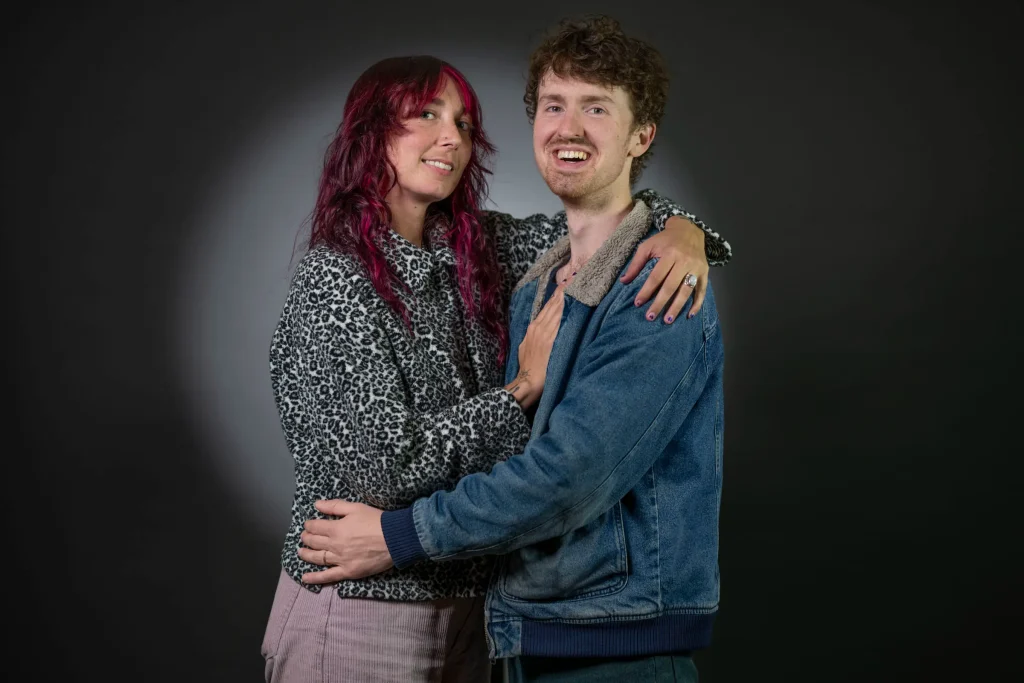 Couple in a studio, she with red-streaked hair, he in a denim jacket