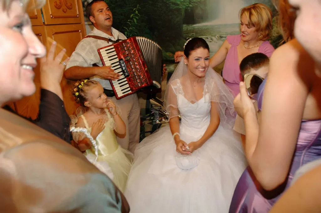 Bride in her veil smiling among guests as an accordion player sings