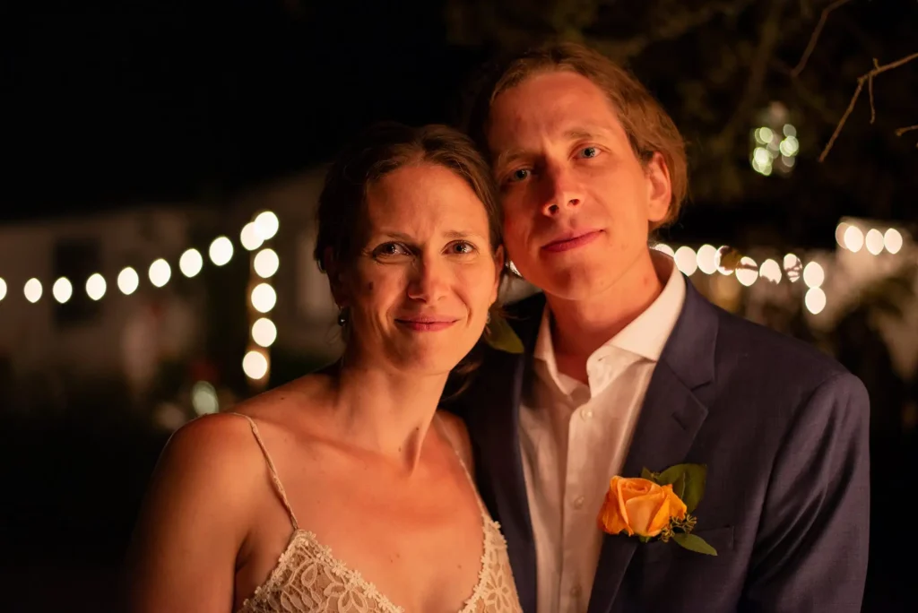Bride and groom at night with string lights behind them